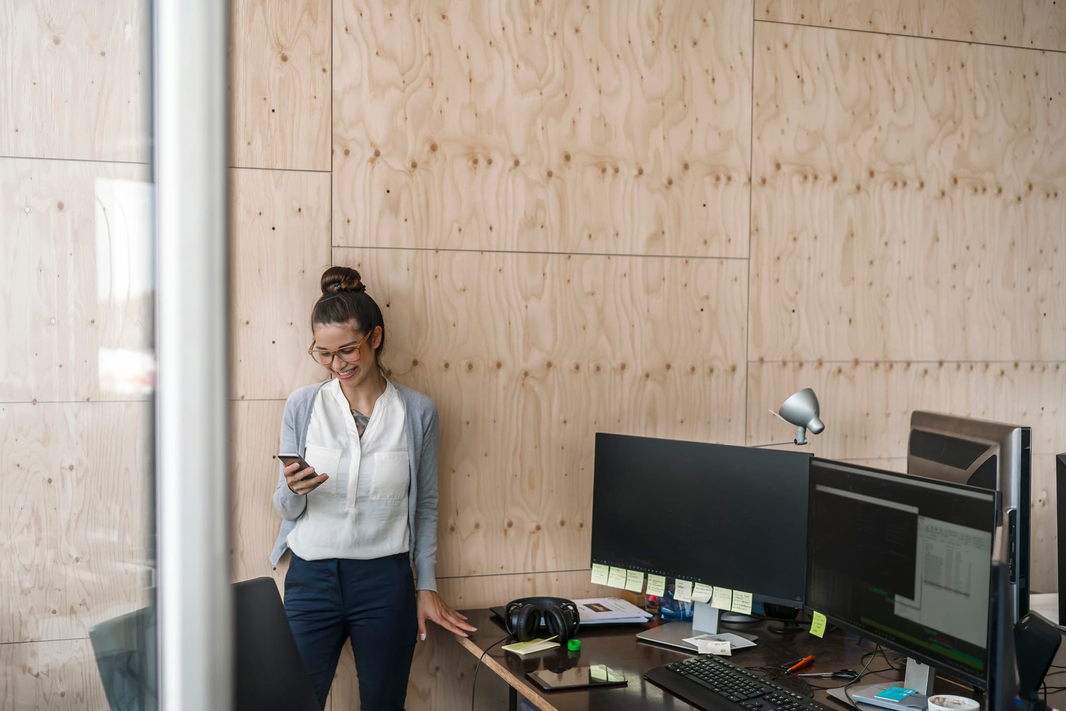 Young woman working in office, using smaftphone, laughing