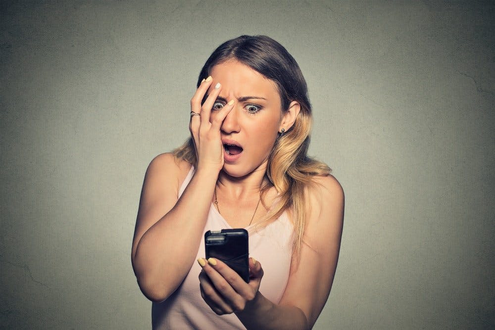 Closeup portrait anxious scared young girl looking at phone seeing bad news photos message with disgusting emotion on her face isolated on gray wall background. Human reaction expression