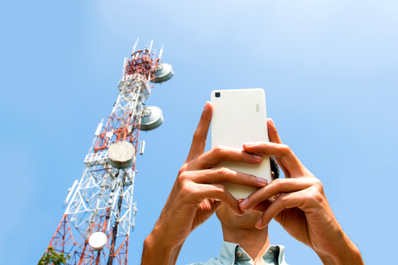 a man uses a smartphone with a telecommunication tower in the background