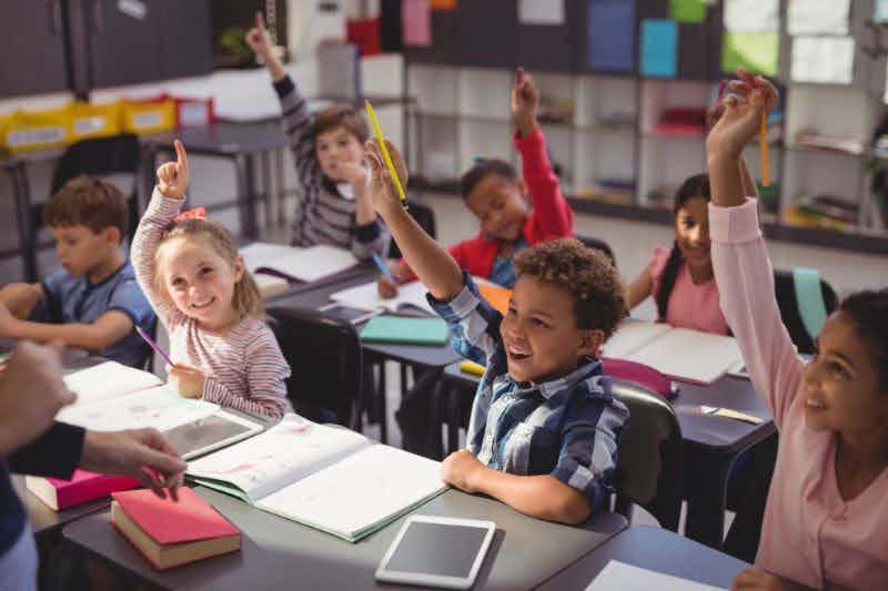primary school children raising their hands in a classroom