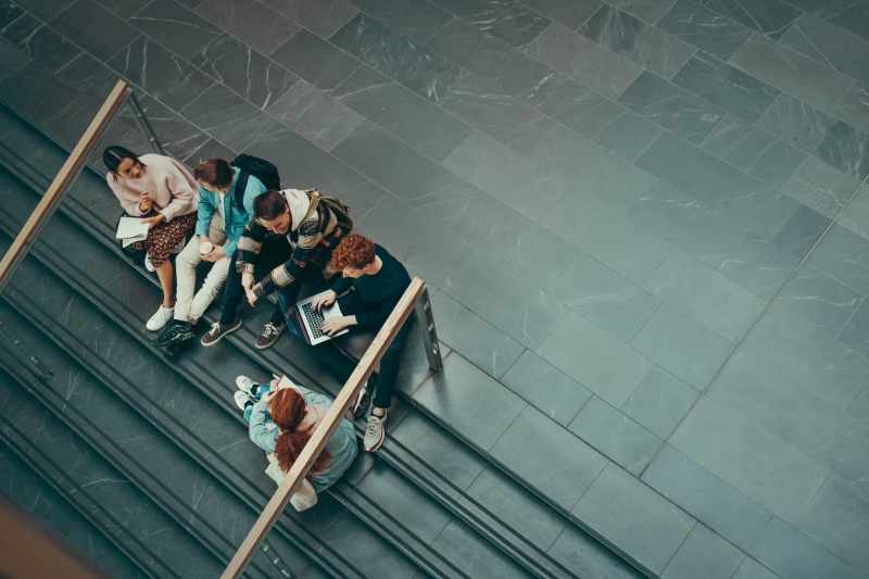 High angle view of university students sitting on stairs and discussing studies. Young people studying in college campus.