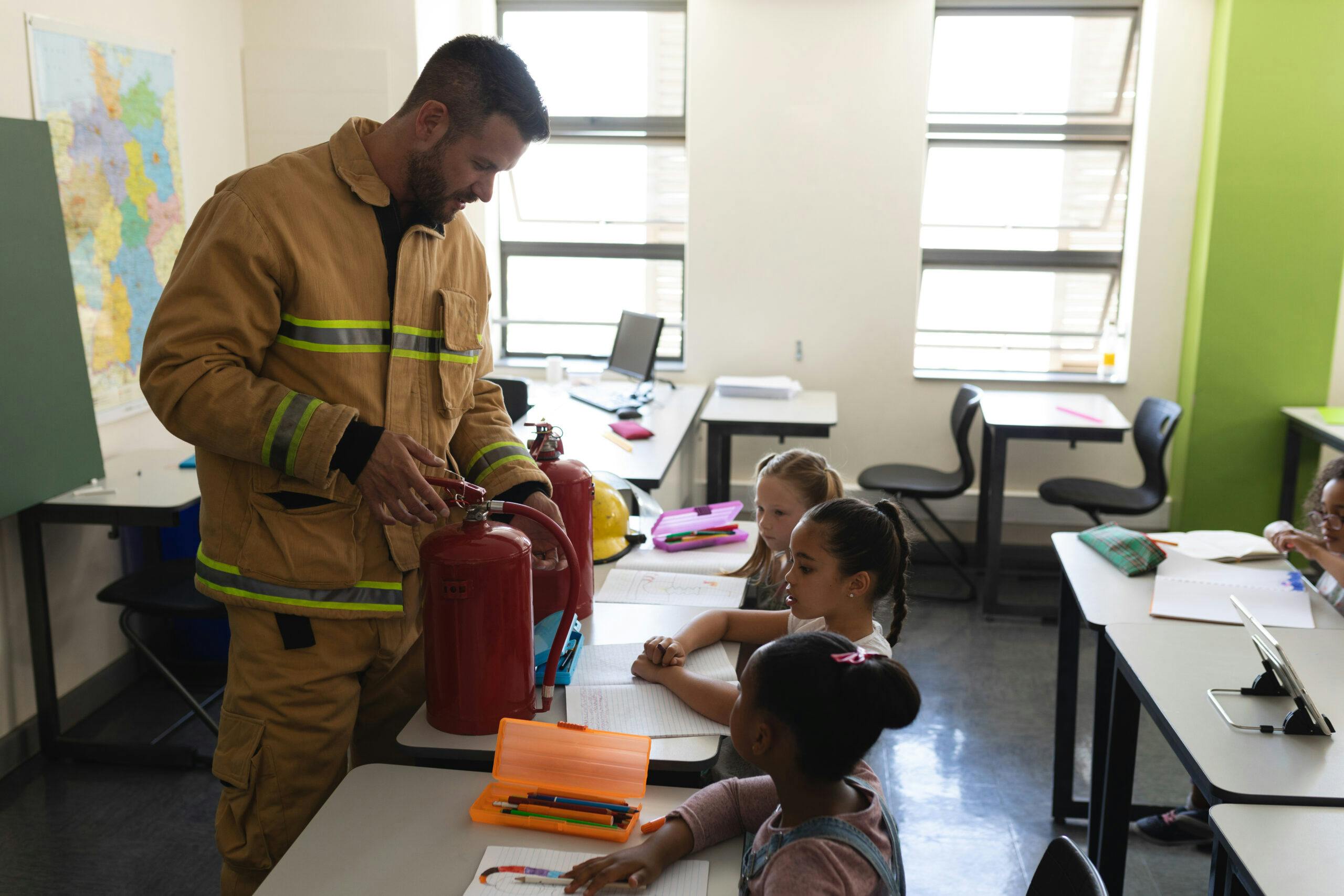 Side view of male Caucasian firefighter teaching schoolkids about fire safety, showing extinguisher in classroom of elementary school