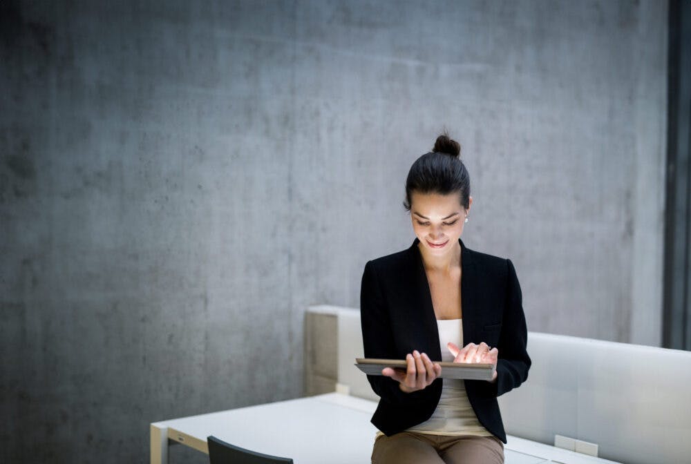 Young student or businesswoman sitting on desk in room in a library or office, using tablet.